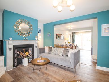 A living room with a gray sofa and a fireplace with a round mirror and flowers at Bay Cottage in Weymouth