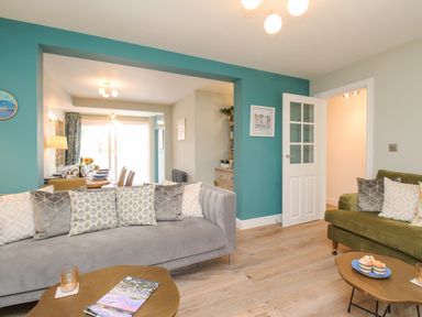 A living room with grey and green sofas a coffee table and a view into a dining area at Bay Cottage in Weymouth