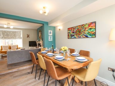 A dining room with a wooden table set for six and a colorful artwork on the wall at Bay Cottage in Weymouth