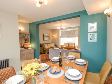 A dining table set with plates glasses and a vase of flowers next to a living room with sofas at Bay Cottage in Weymouth