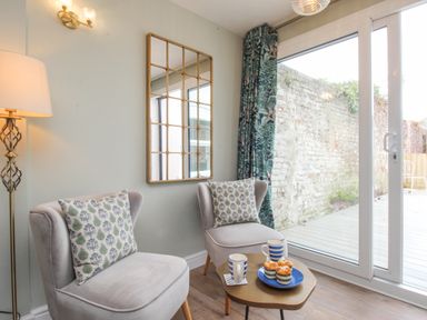 A sitting area with two chairs a small table with cups and muffins next to a glass door at Bay Cottage in Weymouth