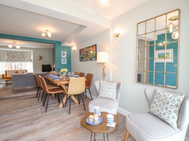 A dining area with a table set for six and two chairs with pillows near a mirror at Bay Cottage in Weymouth