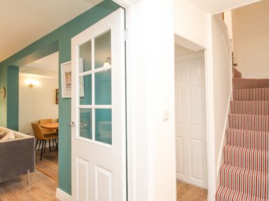 A hallway with striped carpeted stairs and a partially open door showing a dining area at Bay Cottage in Weymouth
