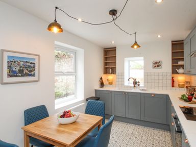 A kitchen with a wooden dining table blue chairs grey cabinets and patterned floor tiles at Bay Cottage in Weymouth