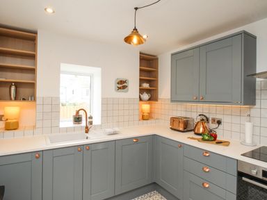 A kitchen with gray cabinets a white countertop a copper faucet a window two lamps a toaster and a kettle at Bay Cottage in Weymouth