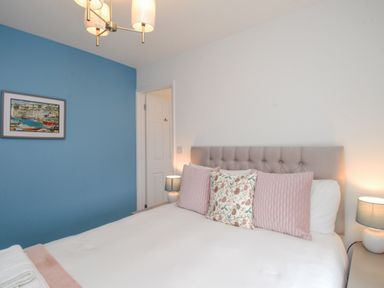 A bedroom with a bed featuring decorative pillows a blue accent wall a framed picture bedside lamps and a ceiling light at Bay Cottage in Weymouth