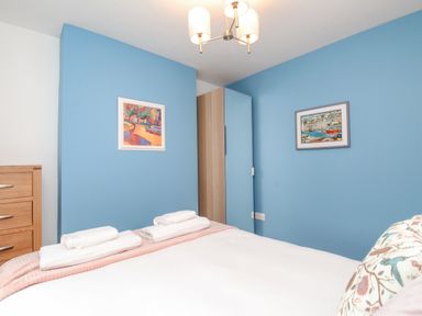 A bedroom with blue walls a bed with folded towels a wooden chest of drawers and two framed paintings at Bay Cottage in Weymouth