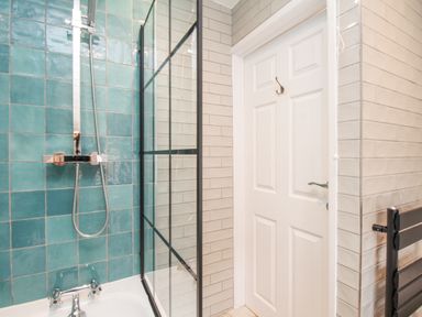A bathroom with turquoise tiles around a bathtub shower and a white door at Bay Cottage in Weymouth