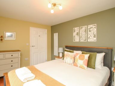 A bedroom with a bed with pillows and towels and a dresser against a yellow wall at Bay Cottage in Weymouth