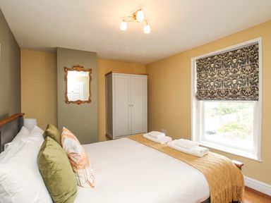A bedroom with a bed, pillows, folded towels on a blanket, a wardrobe, a window with patterned blind, and a mirror on the wall at Bay Cottage in Weymouth