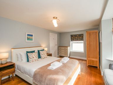 A bedroom with a bed lamps on bedside tables a chest of drawers a wardrobe and a window at Bay Cottage in Weymouth