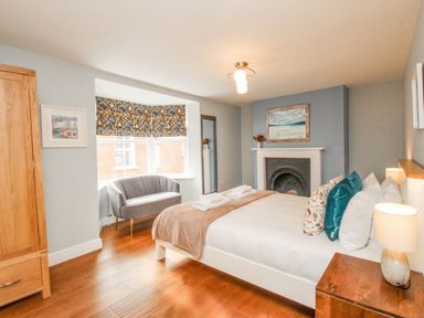 A bedroom with a bed pillows and towels bedside tables a fireplace a sofa and a wooden wardrobe at Bay Cottage in Weymouth