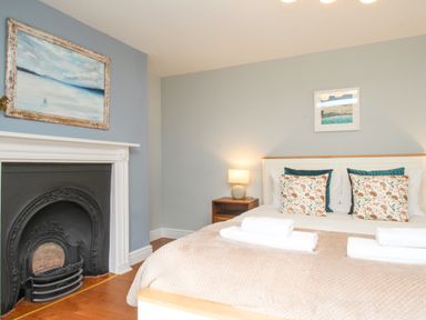 A bedroom with a bed with floral cushions a bedside table with lamp and a fireplace at Bay Cottage in Weymouth