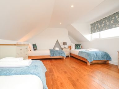 A bedroom with three single beds blue throws pillows and wooden floor at Bay Cottage in Weymouth
