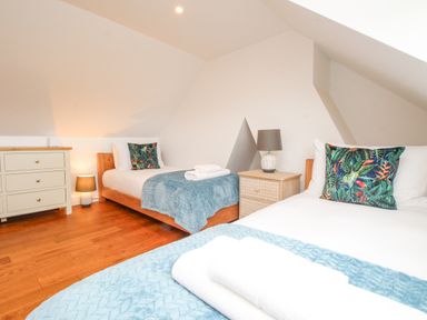 A bedroom with two single beds blue throws pillows with leaf patterns a chest of drawers and two bedside tables with lamps at Bay Cottage in Weymouth