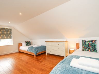 A bedroom with two single beds a white dresser a window with a patterned blind and wooden floor at Bay Cottage in Weymouth