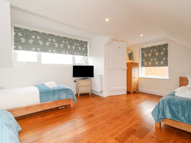 A bedroom with two single beds a television on a small cabinet and wooden flooring at Bay Cottage in Weymouth