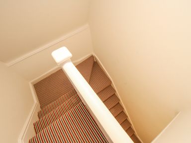A stairway with striped carpet and white walls and banister at Bay Cottage in Weymouth