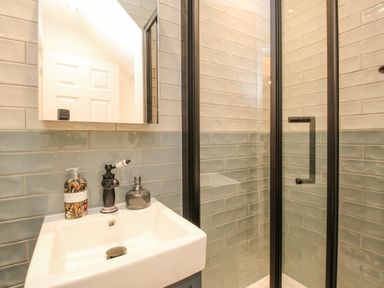 A bathroom with a sink a mirror and a shower with a glass door at Bay Cottage in Weymouth