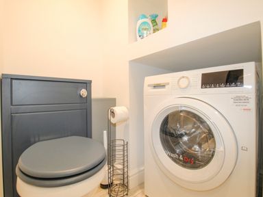 A bathroom with a toilet and a washing machine along with cleaning supplies on a shelf at Bay Cottage in Weymouth