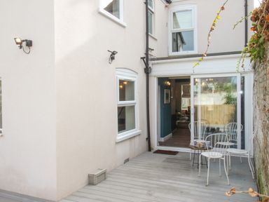 A small outdoor patio with white metal chairs and a table in front of sliding glass doors at Bay Cottage in Weymouth