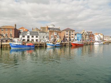 A harbor with boats docked next to buildings along the waterfront at Bay Cottage in Weymouth