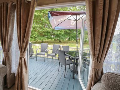 A patio with four chairs a table and an umbrella visible through open doors with curtains at Stanley's Lodge Foxburrow Hang Belton Norfolk