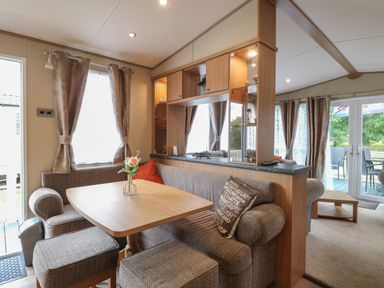 A dining area with a wooden table and cushioned seating next to windows with curtains at Stanley's Lodge Foxburrow Hang in Belton Norfolk