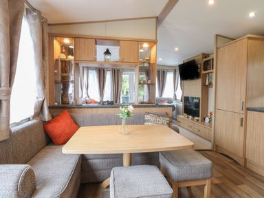 A dining area with a wooden table, upholstered seating, cushions, and a small vase with flowers at Stanley's Lodge, Foxburrow Hang in Belton, Norfolk
