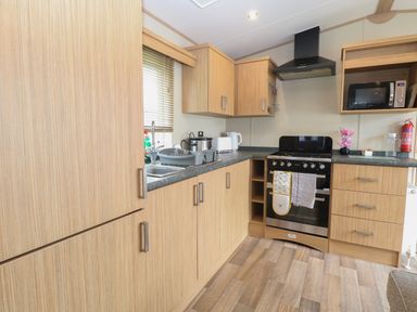 A kitchen with wooden cabinets, a stove, microwave, sink, and countertop appliances at Stanleys Lodge Foxburrow Hang in Belton Norfolk