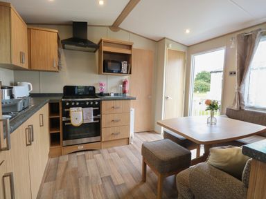 A kitchen and dining area with wooden cabinets and a table with a flower vase at Stanley's Lodge Foxburrow Hang in Belton Norfolk