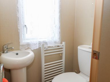 A small bathroom with a pedestal sink toilet window with lace curtain and a white towel radiator at Stanleys Lodge Foxburrow Hang in Belton Norfolk