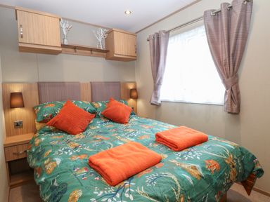 A bedroom with a double bed green patterned bedding orange pillows and towels beside a window with curtains at Stanleys Lodge Foxburrow Hang in Belton Norfolk