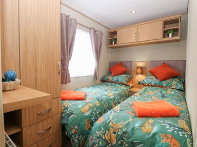 A bedroom with two single beds with patterned bedding and orange towels at Stanley's Lodge Foxburrow Hang in Belton Norfolk
