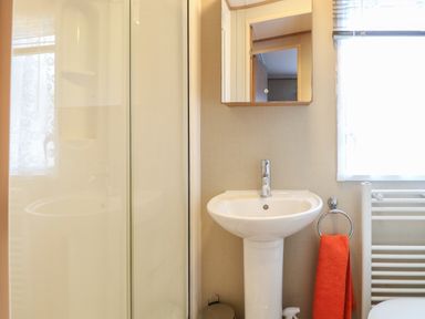 A bathroom with a white pedestal sink a mirror above a towel ring with a red towel a window with blinds and a white radiator at Stanleys Lodge Foxburrow Hang in Belton Norfolk