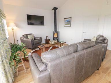 A living room with leather sofas a wood stove a wall mounted tv and a plant at Heritage Retreat in Monknash