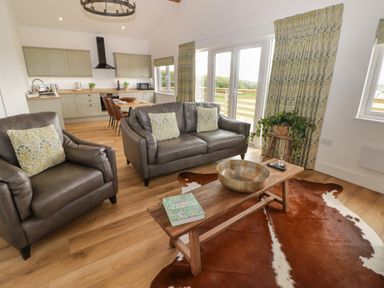 A living area with leather armchair and sofa with cushions wooden coffee table and kitchen area at Heritage Retreat in Monknash