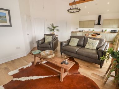 A living area with a leather sofa and armchair a wooden coffee table on a cowhide rug a kitchen with cabinets and appliances at Heritage Retreat Monknash