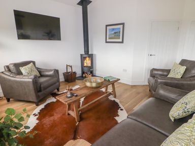 A living room with leather sofas wooden coffee table wood stove and mounted TV at Heritage Retreat in Monknash
