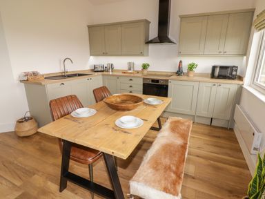 A kitchen with grey cabinets wooden table brown chairs and a bench at Heritage Retreat in Monknash