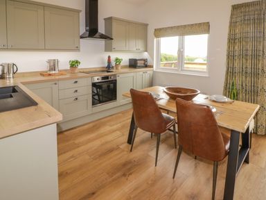 A kitchen with wooden floors a wooden table with two chairs and green cabinets at Heritage Retreat in Monknash