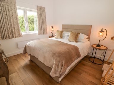 A bedroom with a double bed bedside tables lamps curtains and wooden floor at Heritage Retreat in Monknash
