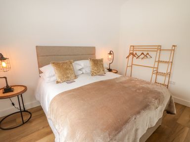 A bedroom with a bed table lamps and a wooden clothes rack at Heritage Retreat in Monknash