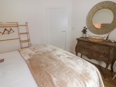 A bedroom with a beige blanket on the bed a wooden chest of drawers with a round mirror and a clothes rack with hangers at Heritage Retreat Monknash