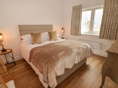 A bedroom with a double bed two bedside tables with lamps floral curtains and wooden floor at Heritage Retreat in Monknash