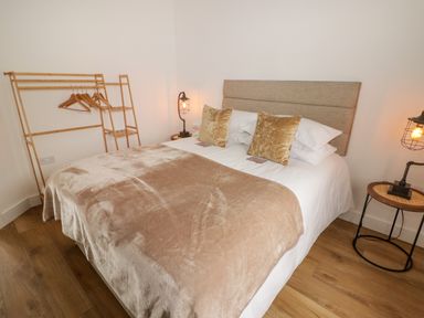 A bedroom with a bed covered with pillows and a blanket next to bedside tables with lamps and a wooden clothes rack at Heritage Retreat in Monknash