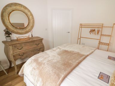 A bedroom with a wooden dresser and round mirror a bed with beige blanket and a wooden clothes rack at Heritage Retreat in Monknash