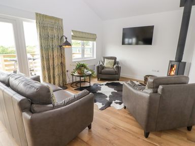A living room with leather sofas a round table with plant a wood burning stove and a wall mounted television at Monks Rest in Monknash