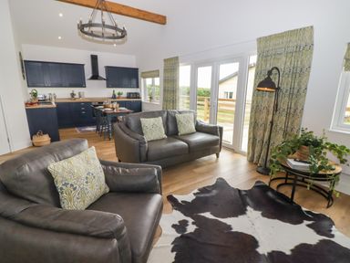A living room with a leather armchair and sofa a cowhide rug and curtains next to a kitchen with a dining table at Monks Rest in Monknash