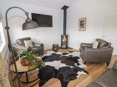 A living room with two leather chairs a wood burning stove a wall mounted television and a cowhide rug at Monks Rest in Monknash